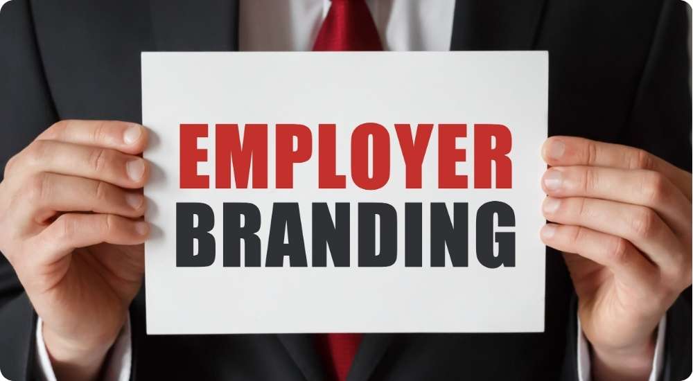 A close-up photograph of a business professional in a suit holding a white sign with the words "EMPLOYER BRANDING" written in bold red and black text.
