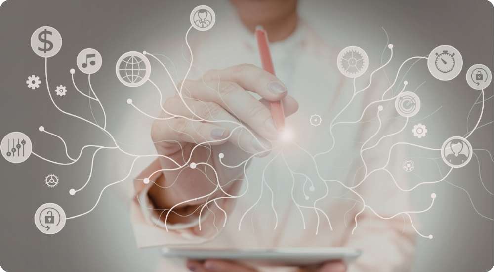 A person uses a stylus on a digital tablet to connect various glowing business icons, including symbols for money, music, a globe, and security locks, illustrating the integration of business functions for strategy and innovation.