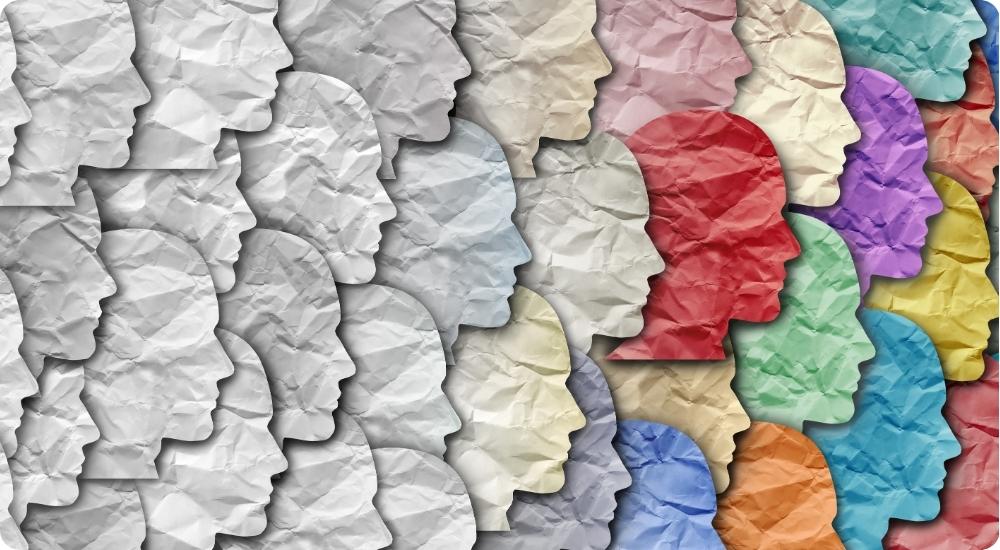 Diversity and inclusion concept showing multiple colorful human profile silhouettes made of crumpled paper and one red paper cutout head among them, representing unique talent, individuality, or standing out from the crowd.