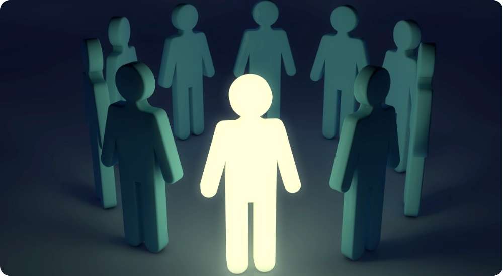 A single bright, glowing human figure stands in the center of a circle of darker figures, illustrating a leadership, innovation, or change metaphor.