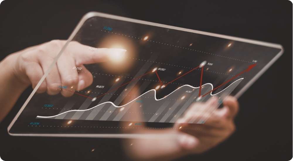 A person interacts with a transparent digital tablet displaying data analytics charts and graphs with an upward trend line, symbolizing the analysis of technology workforce trends.