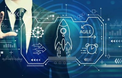 A business professional interacts with a blue and white digital interface that includes icons for a rocket taking off, gears, a clock, and the word AGILE, symbolizing the development and implementation of agile technology strategies.