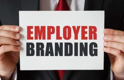 A close-up photograph of a business professional in a suit holding a white sign with the words "EMPLOYER BRANDING" written in bold red and black text.