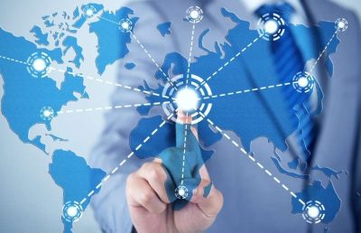 A close-up photograph of a business professional pointing a finger at a glowing network hub overlaid on a digital world map, symbolizing the challenges of managing global compliance.