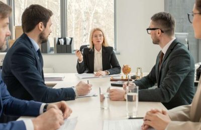 A group of diverse professionals in formal business attire sitting around a conference table during a meeting, representing a team collaborating on hiring roadmaps and strategic workforce planning for a modern tech firm.