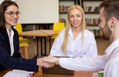 A close-up shot of a male and female business professional shaking hands across a conference table with open notebooks, symbolizing a successful partnership, a signed agreement, or a new employee being welcomed to a leadership team.