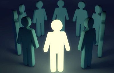 A single bright, glowing human figure stands in the center of a circle of darker figures, illustrating a leadership, innovation, or change metaphor.