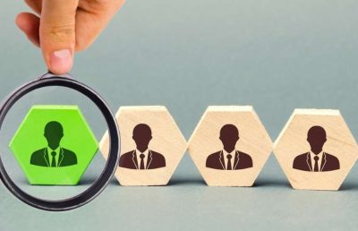 Magnifying glass highlights a green hexagon with a person icon from a line of grey hexagon employee blocks.