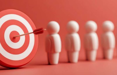 A close-up photograph of a red and white bullseye target with an arrow hitting the center, positioned next to a line of generic human figures, symbolizing talent retention success.