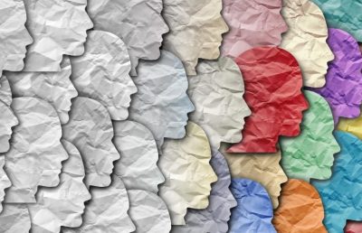 Diversity and inclusion concept showing multiple colorful human profile silhouettes made of crumpled paper and one red paper cutout head among them, representing unique talent, individuality, or standing out from the crowd.